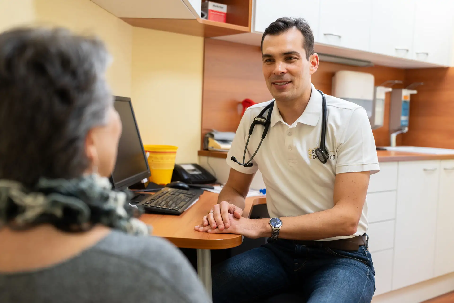 Arzt im Gespräch mit einer älteren Patientin an seinem Schreibtisch