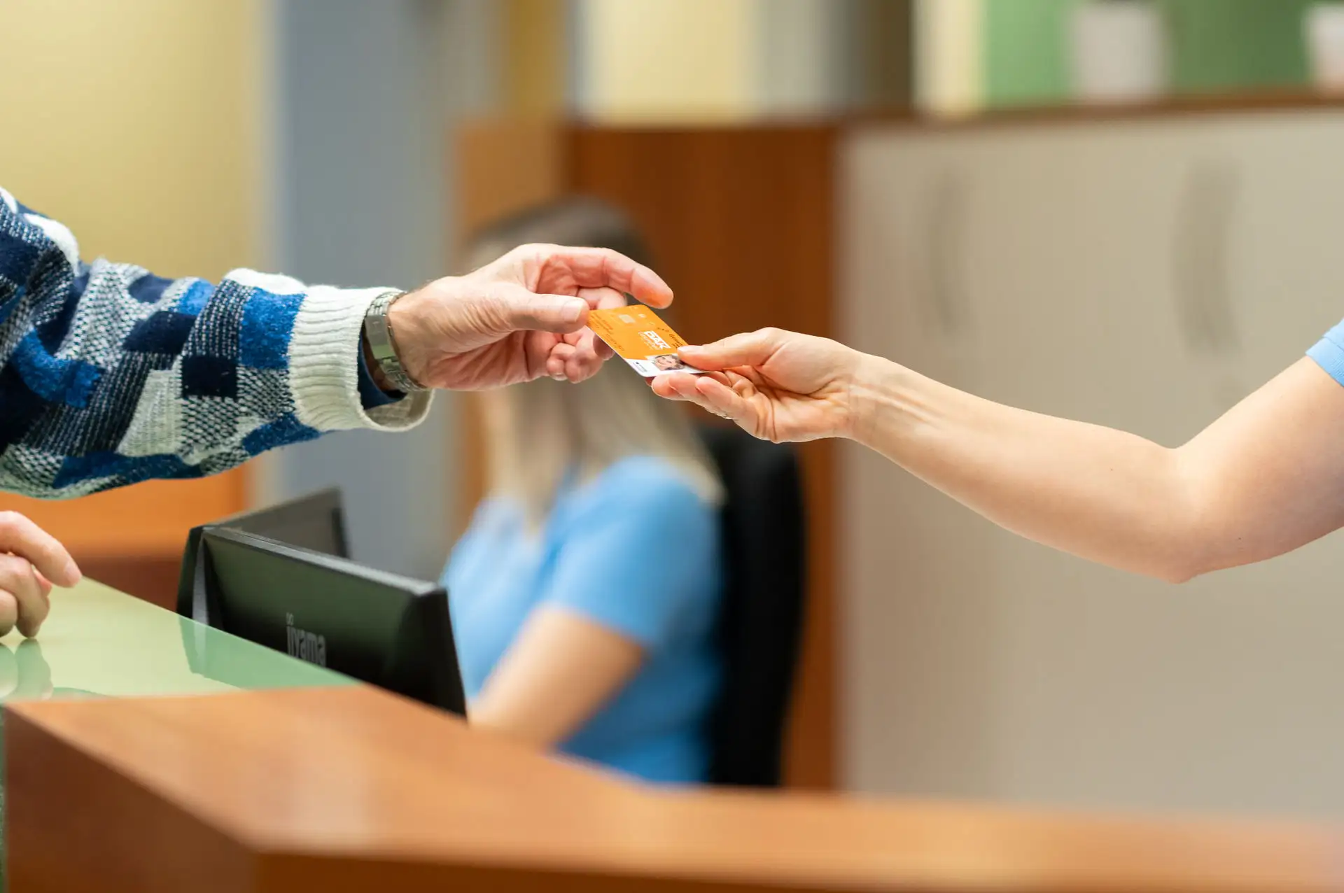 Patient überreicht einer MFA an der Rezeption seine Krankenkassenkarte